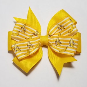 May include: A yellow hair bow with a white and yellow striped ribbon featuring a banana print.