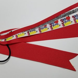 May include: Red, white, and yellow ribbon hair tie with a silver glitter ribbon. The ribbon has a repeating pattern of pencils, apples, and the text "3rd grade".