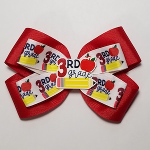 May include: Red and white hair bow with a pencil and apple design. The bow has the text "3rd grade" on it.