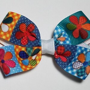 May include: A colorful hair bow with a floral pattern in shades of blue, red, yellow, orange, and green. The bow is tied with a white ribbon.