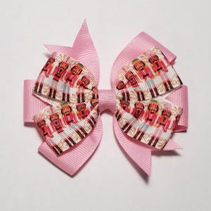 May include: A pink hair bow with a white ribbon featuring a repeating pattern of nutcracker figures.