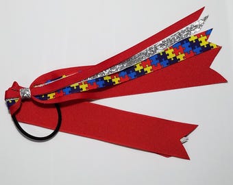 May include: Red ribbon hair tie with a bow and a silver glitter ribbon, a blue ribbon with a puzzle piece pattern, and a yellow ribbon with a puzzle piece pattern.