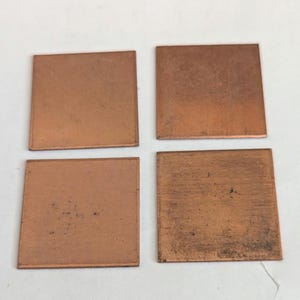 May include: Four flat, square-shaped copper plates arranged in a two-by-two grid. Each plate features a metallic, reddish-brown surface with subtle variations in texture and tone, showing a natural, unpolished finish across all four pieces.