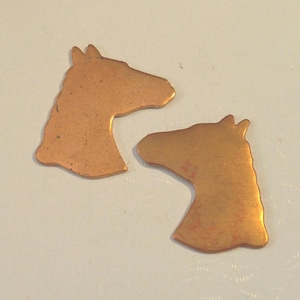 May include: Two copper horse head silhouettes. The horse heads are cut out of copper sheet metal and have a rustic, aged look.