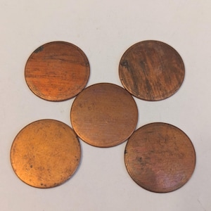 May include: Five round copper discs, each with a slightly different patina, arranged in a star shape on a white background.