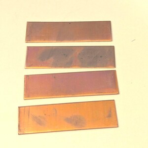 May include: Four rectangular copper sheets with varying shades of orange, brown, and purple. The sheets are arranged vertically, with the darkest sheet at the top and the lightest sheet at the bottom.