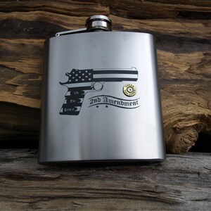 May include: A stainless steel hip flask featuring a black and white handgun graphic with an American flag design. The text "2nd Amendment" is below the gun. A bullet is next to the gun.