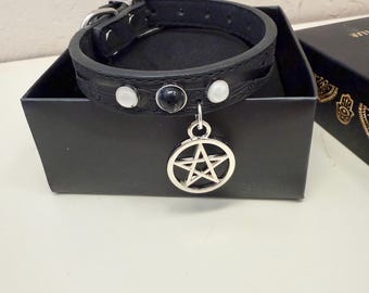 May include: Black leather choker with silver buckle and a silver pentagram pendant. The choker features three decorative stones: two white and one black. The choker is displayed in a black box.