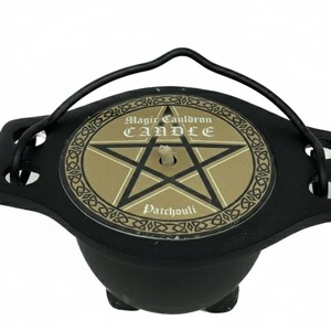 May include: Black cauldron-shaped candle with a handle. The candle has a gold-colored top with a pentagram design and the words "Magic Cauldron CANDLE" and "Patchouli". The cauldron has three small feet.