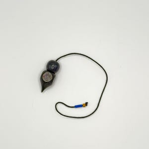 May include: A black wooden pendulum with a circular design and a black string. The string has a blue and gold bead at the end.