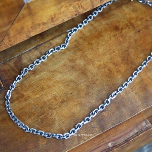 May include: A silver chain necklace on a wooden surface. The chain is made of small, linked oval shapes.