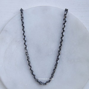 May include: A silver chain necklace with a box chain design. The chain is on a white surface.