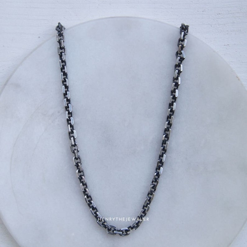 May include: A silver chain necklace with a box chain design. The chain is on a white surface.