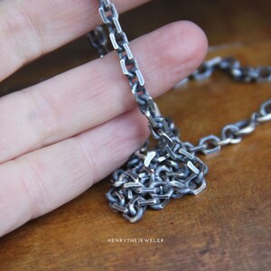 May include: A silver chain necklace with a box chain design. The chain is made of thick, flat links.