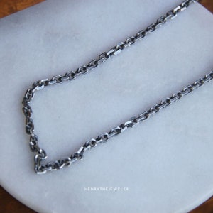 May include: A silver chain necklace with a box chain design. The chain is on a white surface.