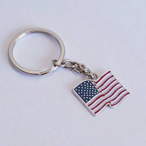 May include: A silver key chain with a small American flag charm. The flag is red, white, and blue with stars on the blue field.