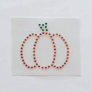 Peut inclure: Gros plan sur une citrouille faite de strass orange et verts sur un fond blanc.