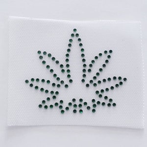 May include: A white fabric patch with a green rhinestone marijuana leaf design.