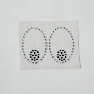 May include: A white fabric patch with two silver rhinestone circles and two black rhinestone circles in the centre of each circle.