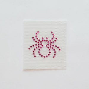 May include: A white fabric patch with a pink rhinestone design of a crab.