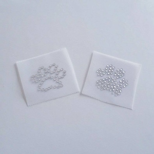 May include: Two white fabric patches with silver rhinestone paw prints. The paw prints are different sizes and shapes.