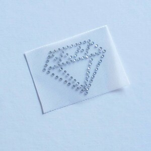 May include: A white fabric patch with a silver diamond shape made of rhinestones.