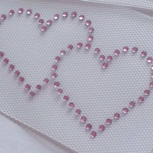 May include: Two pink rhinestone hearts on a white fabric background.