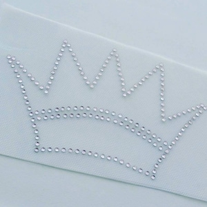 May include: A crown design made of clear rhinestones on a light blue background.