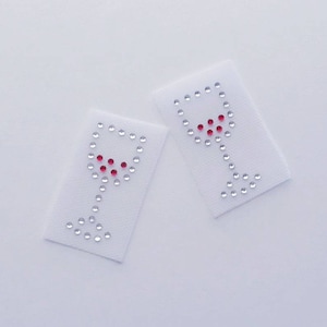 May include: Two white fabric patches with a wine glass design made of silver and red rhinestones.