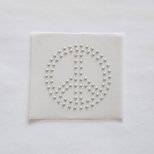 May include: A white fabric patch with a silver peace sign made of rhinestones.
