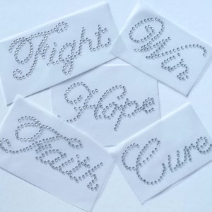 May include: Five white fabric patches with the words "The Night", "Forever", "Sweet", "Love", and "Cure" spelled out in silver rhinestones.
