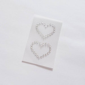 May include: Two white heart shapes made of rhinestones on a white mesh fabric.
