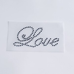May include: A white fabric patch with the word "Love" spelled out in black rhinestones.