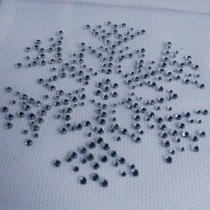 May include: A snowflake design made of numerous small, clear, round rhinestones. The rhinestones are arranged on a white, textured fabric, creating a sparkling, winter-themed pattern. The rhinestones vary slightly in size and reflect light.