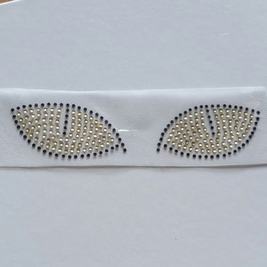 K&ouml;nnte beinhalten: Zwei goldene Strass-Blattformen auf wei&szlig;em Hintergrund. Die Strasssteine sind in Blattform mit schwarzem Umriss angeordnet.