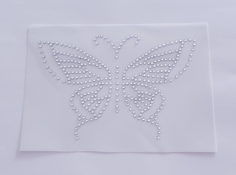 May include: A white fabric patch with a clear rhinestone butterfly design.