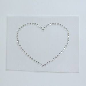 May include: A white fabric with a heart shape outlined with small silver rhinestones.