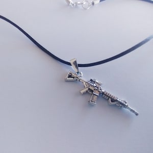 May include: A silver-colored rifle pendant on a black cord necklace.