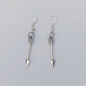 May include: A pair of silver arrow earrings. The arrows are simple and sleek, with a pointed tip and a small loop at the top. The earrings are suspended from silver hooks.