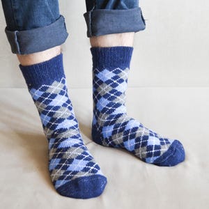 May include: A pair of mid-calf knit socks featuring a classic argyle pattern in shades of navy blue, light blue, and grey. The socks have a ribbed cuff at the top and a solid navy blue toe and heel section, providing a textured look and feel.