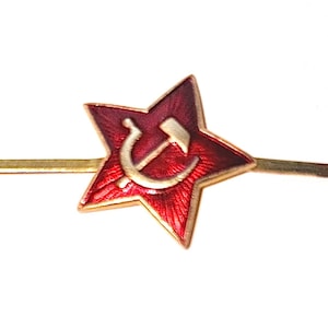 Könnte beinhalten: Eine fünfzackige Sternbrosche mit leuchtend roter Emaille-Oberfläche und einem darunter liegenden, texturierten Strahlenmuster. In der Mitte des Sterns befindet sich ein goldenes Hammer-und-Sichel-Emblem.