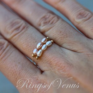 May include: A delicate gold ring with two rows of small, oval-shaped pearls. The pearls are a mix of white and light pink.