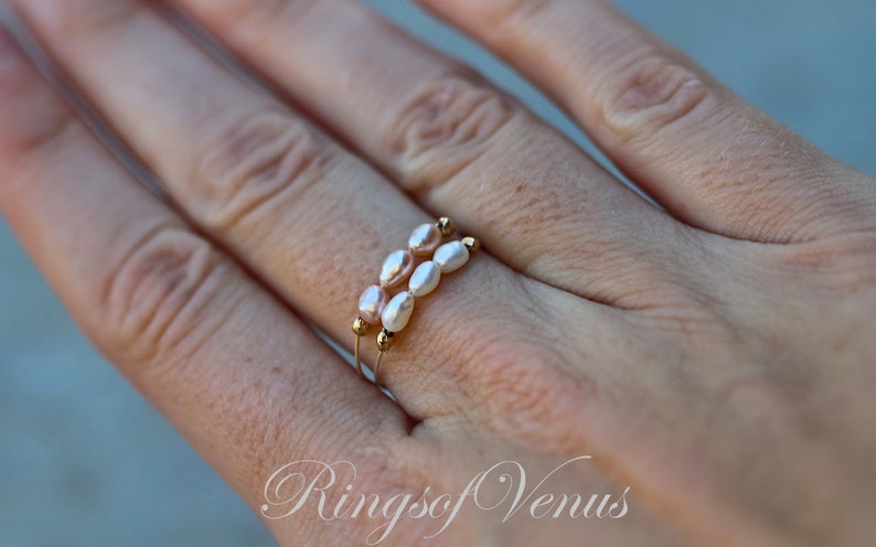 May include: A delicate gold ring with two rows of small, oval-shaped pearls. The pearls are a mix of white and light pink.
