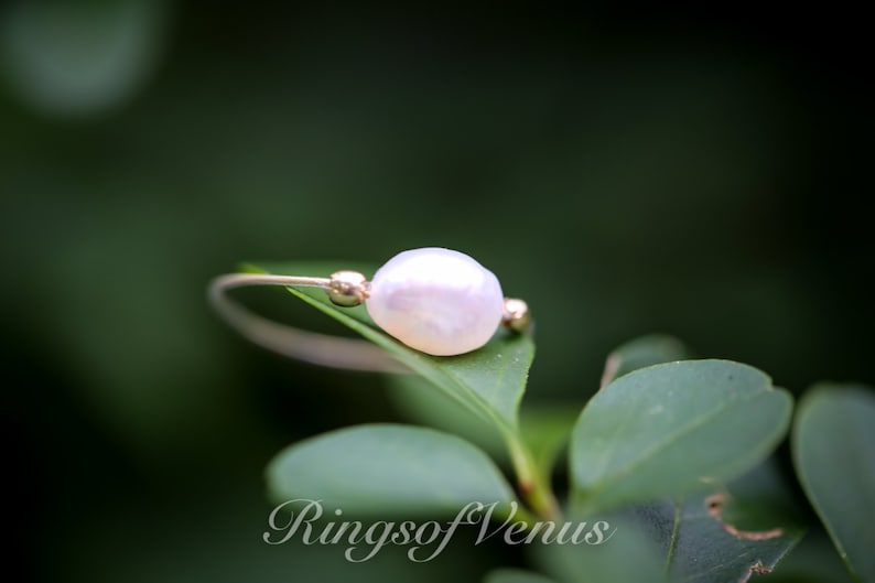 May include: A delicate gold ring featuring a single white pearl, resting on a green leaf. The ring is simple and elegant, ideal for everyday wear.