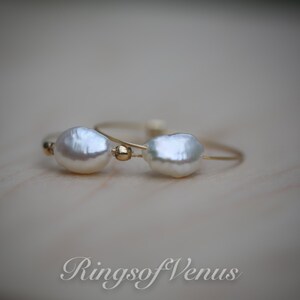 May include: Two delicate gold rings with white baroque pearls. The rings are simple and elegant, perfect for everyday wear.