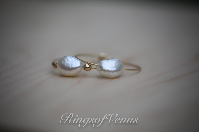May include: Two delicate gold rings with white baroque pearls. The rings are simple and elegant, perfect for everyday wear.