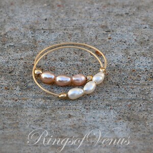 May include: A gold ring with a double band, adorned with a row of five pearls. The pearls are a mix of white and light pink.