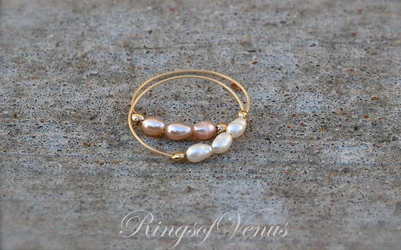 May include: A gold ring with a double band, adorned with a row of five pearls. The pearls are a mix of white and light pink.