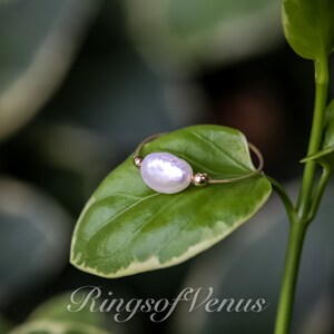 May include: A delicate gold ring featuring a single white pearl, resting on a green leaf. The ring is simple and elegant, ideal for everyday wear.