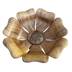 May include: A wooden flower-shaped bowl with seven petals and a detailed centre. The petals are a light brown with darker wood grain patterns. The centre is a darker brown with a carved geometric design.